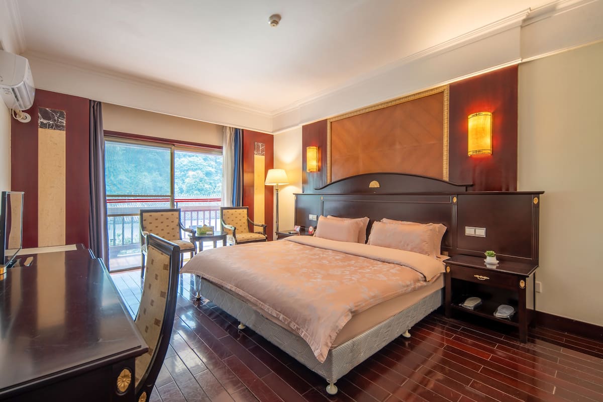 Een hotelkamer met een groot bed, een bureau, een stoel, een klein tafeltje en een raam met uitzicht.