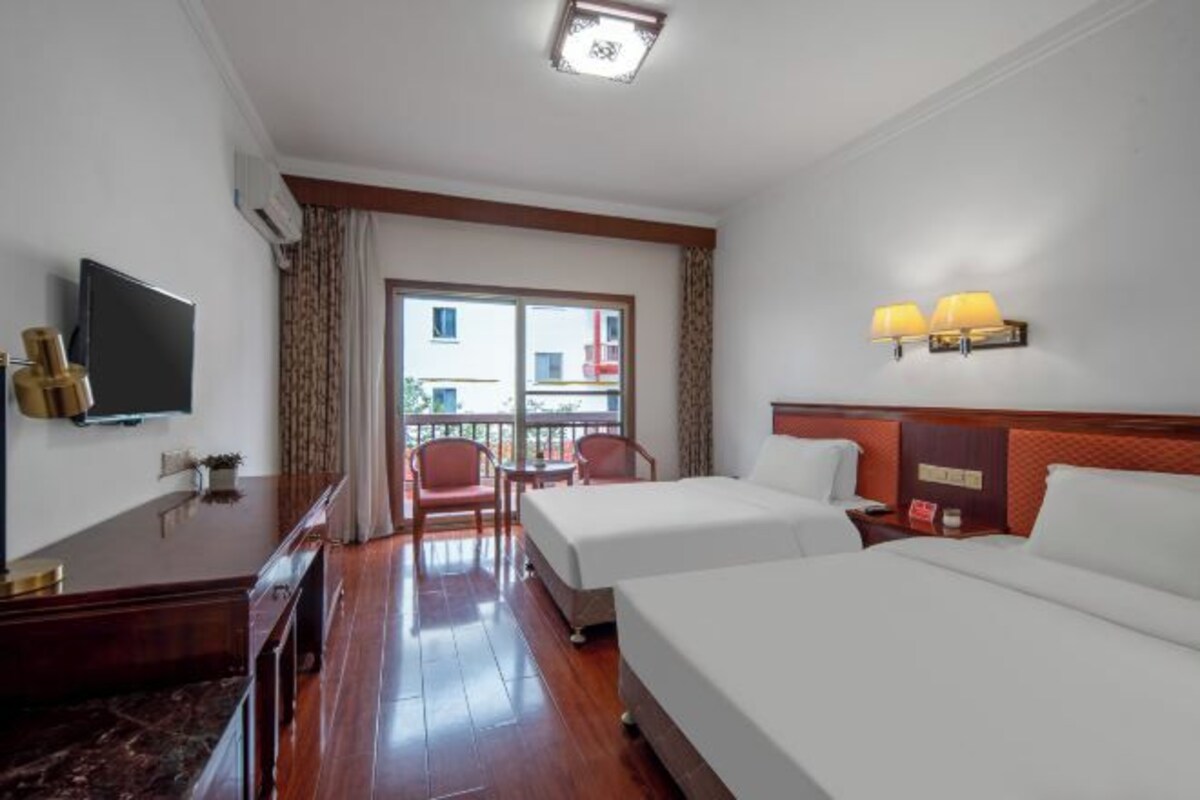 Habitación de hotel con dos camas, televisor, balcón con vistas y escritorio con lámpara.