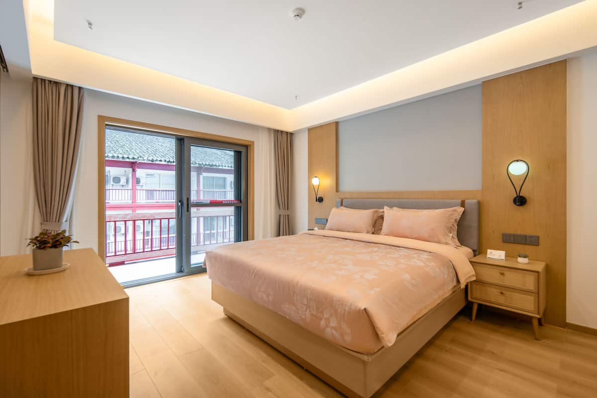 Een moderne slaapkamer met een groot bed, nachtkastjes en uitzicht op een rood gebouw door een schuifdeur.