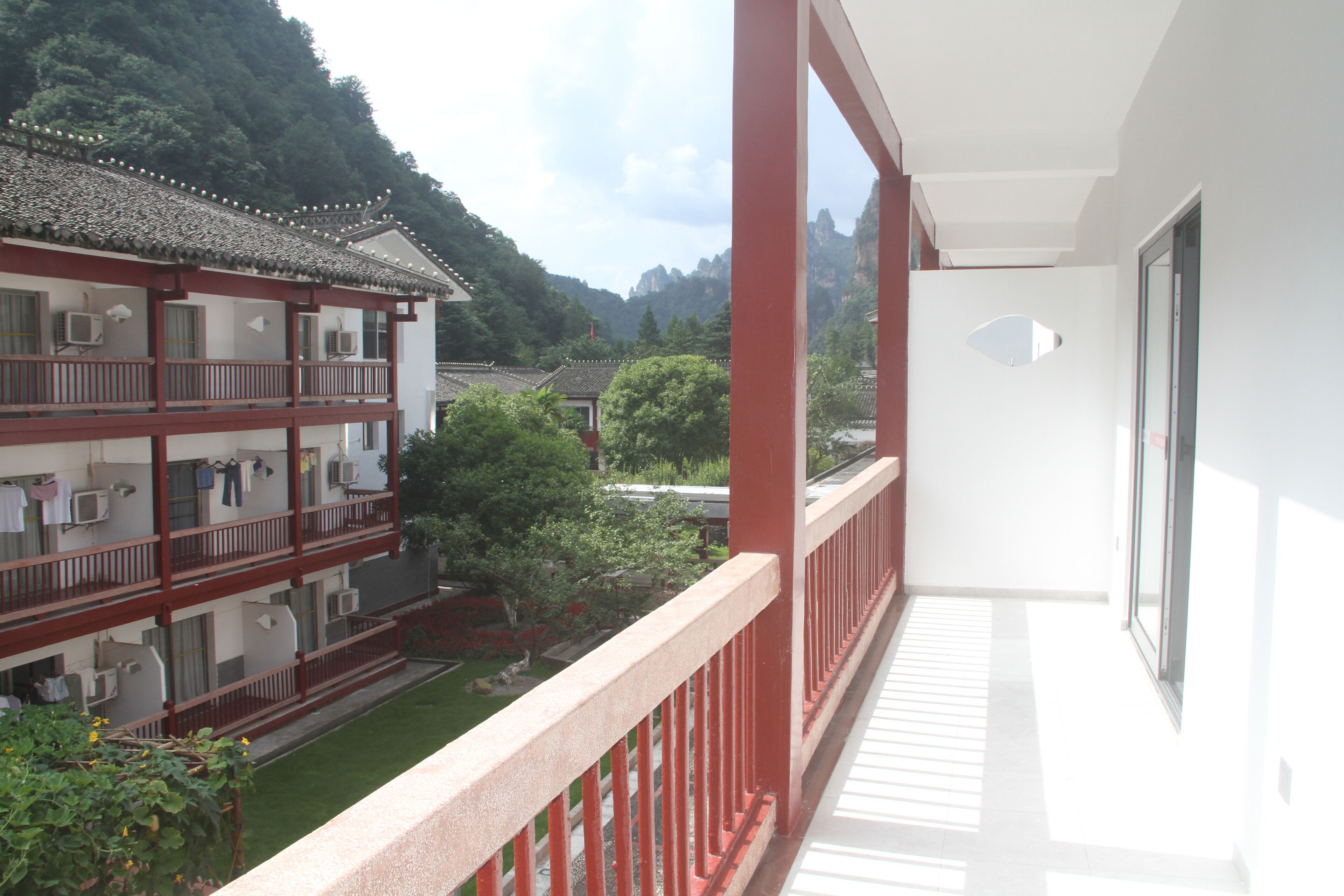 Un edificio de varios pisos con balcones, unidades de aire acondicionado y vistas a un paisaje verde exuberante con árboles y montañas al fondo.