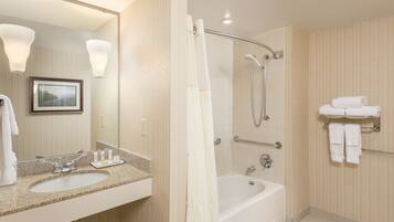 A hotel bathroom with a sink, mirror, framed picture, shower, and towel rack.