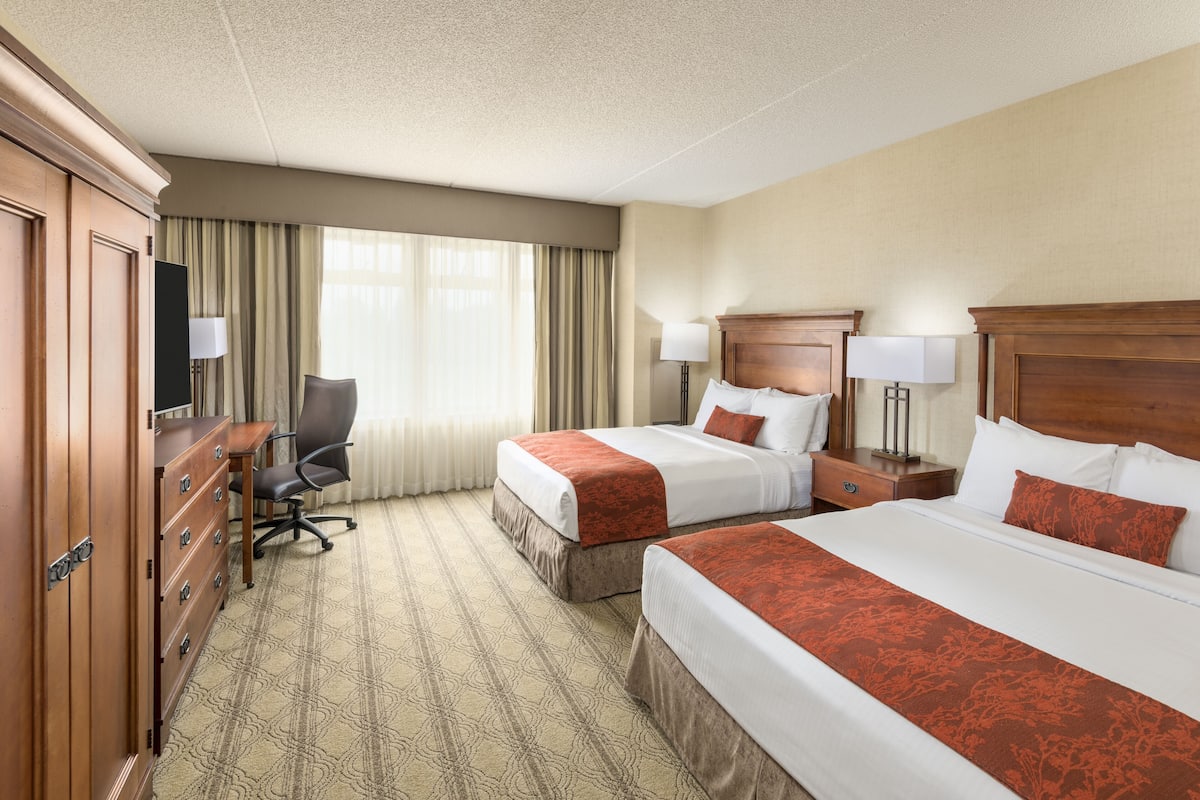 A hotel room with two beds, a desk, a chair, and a dresser.