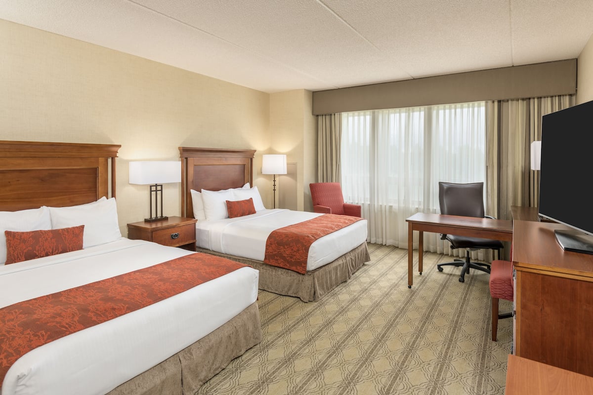 A hotel room with two beds, a desk, a chair, a TV, and a window with curtains.