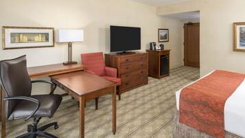 Habitación de hotel con cama, escritorio y silla, televisión, cómoda y puerta que da a otra habitación.