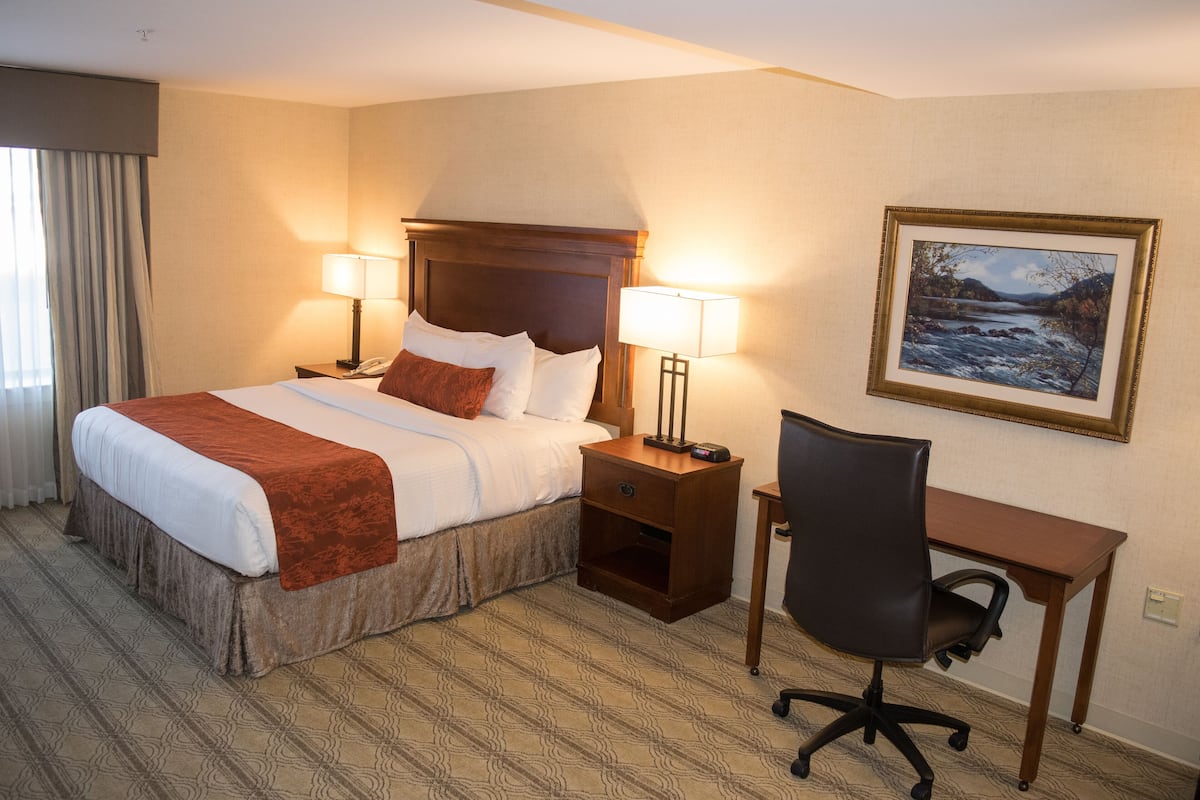 A hotel room with a large bed, two bedside lamps, a desk, and a chair.