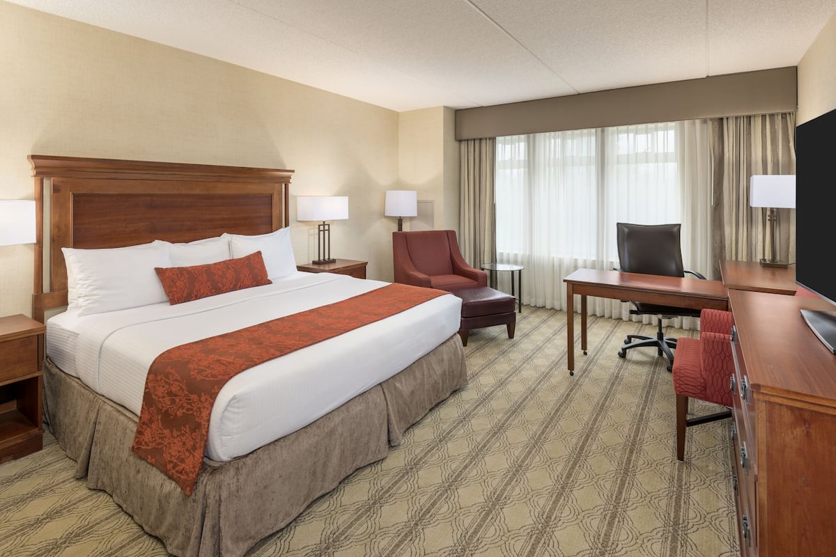 A hotel room with a large bed, a desk, a chair, and a television.