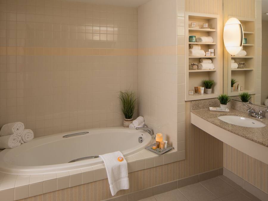 Un baño moderno con una bañera grande, un tocador con lavamanos y un espejo. Hay toallas y artículos de aseo en los estantes.