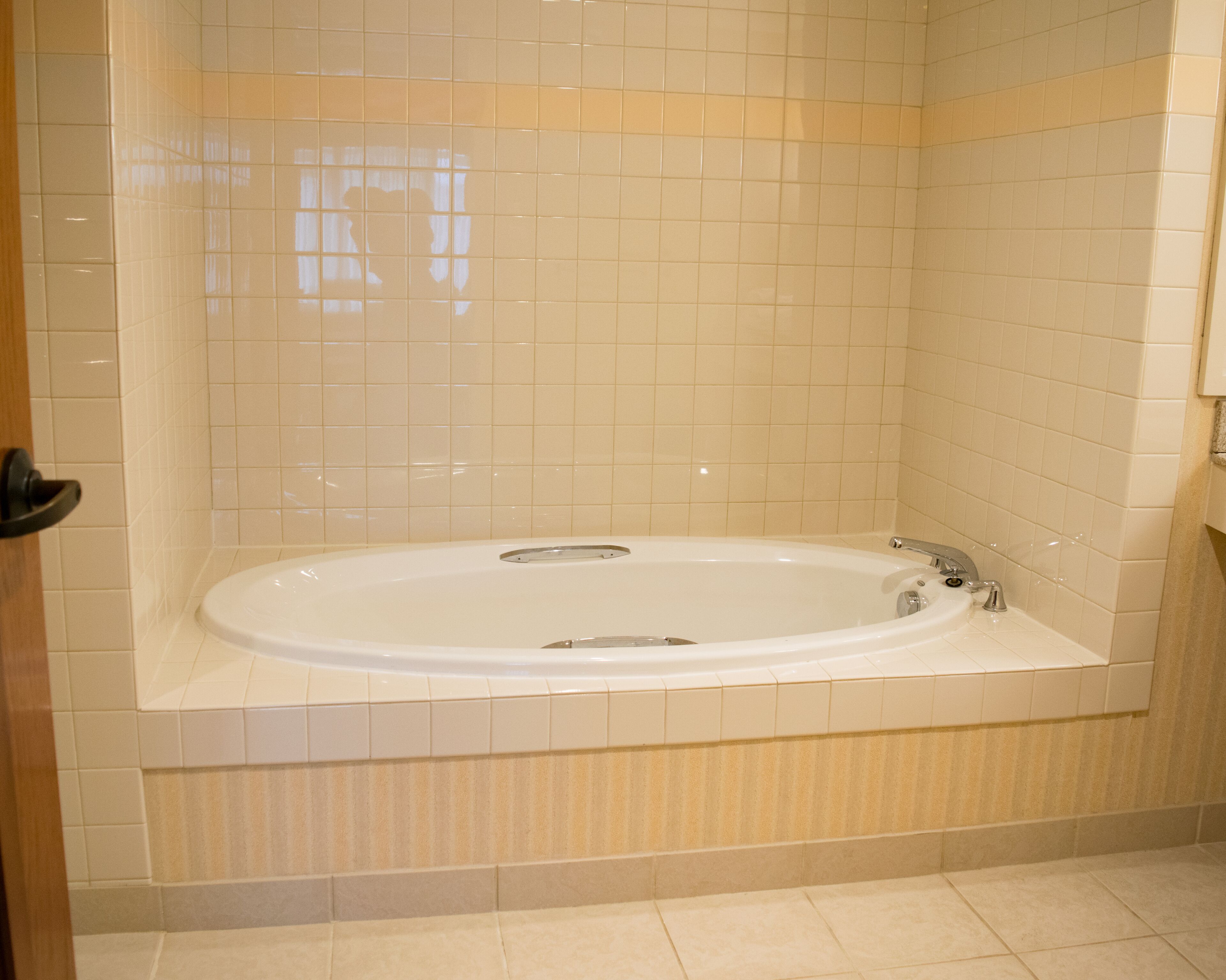 Un baño con una bañera grande, paredes con azulejos y una puerta.