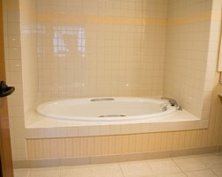 Un baño con una bañera grande, paredes con azulejos y una puerta.