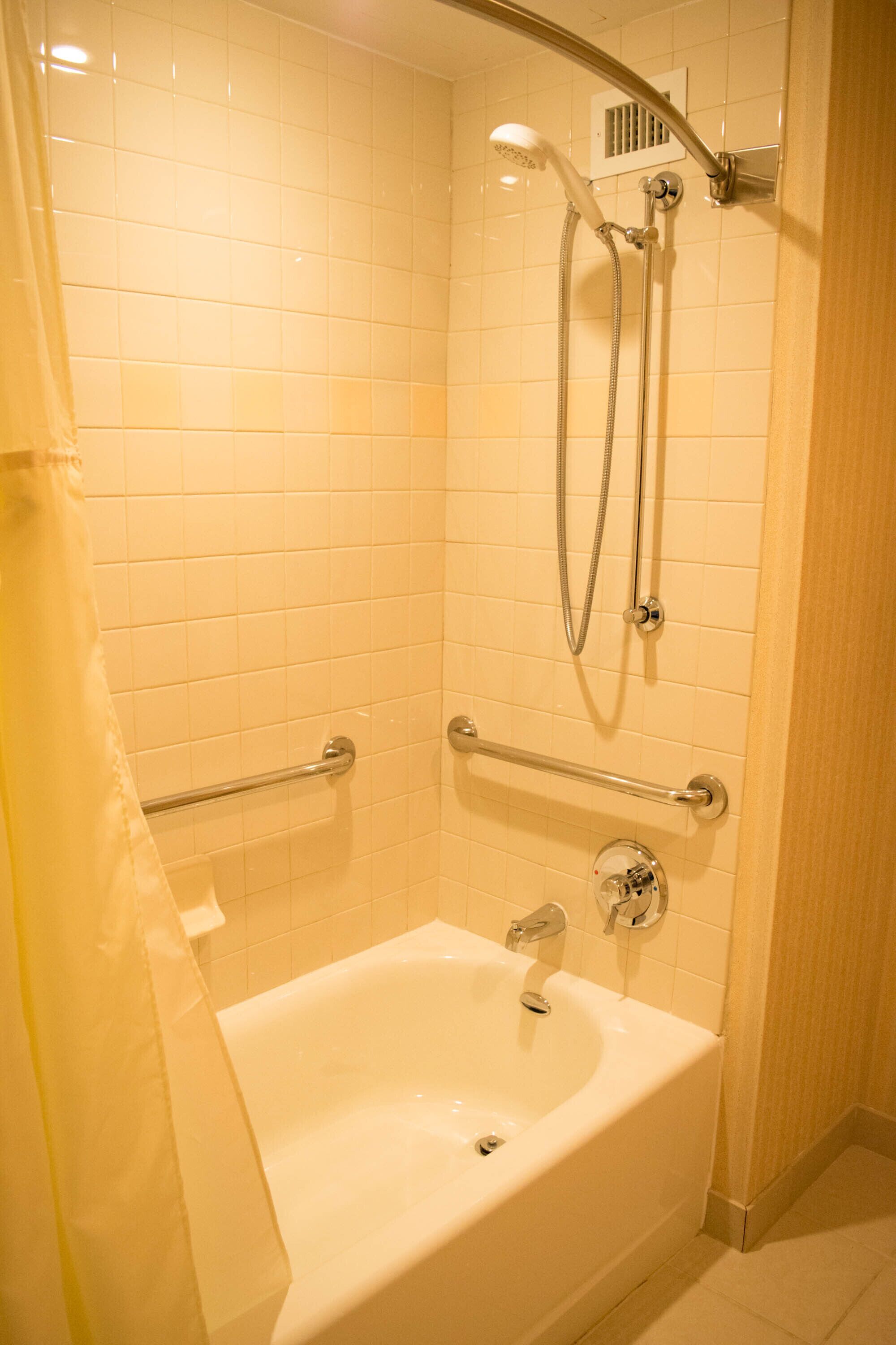 A bathroom with a bathtub, a shower with a handheld showerhead, and grab bars.