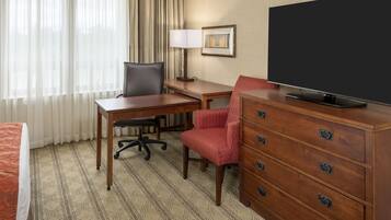 A hotel room with a bed, a desk, a chair, a dresser, a television, and a window with curtains.