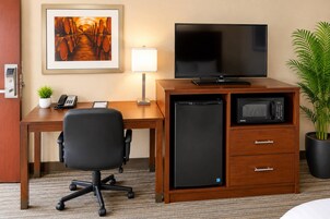 A hotel room with a desk, chair, television, microwave, and a potted plant.
