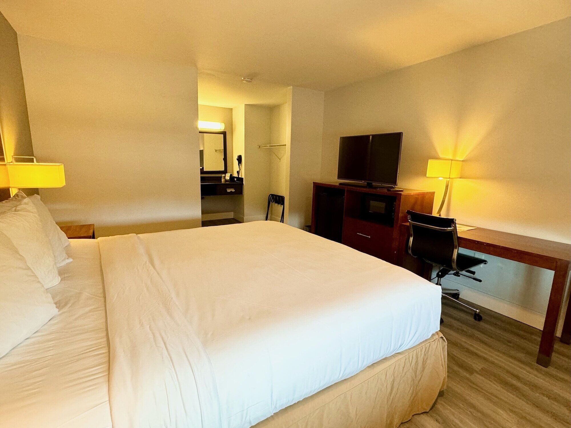 A hotel room with a large bed, a desk with a chair, a television, and a mirror.