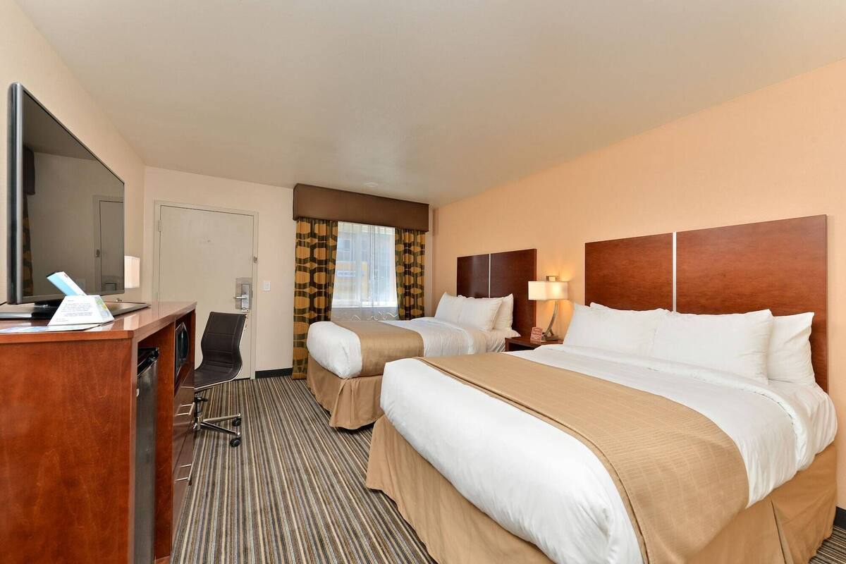 Habitación de hotel con dos camas, un escritorio con computadora, televisión y ventana con cortinas.