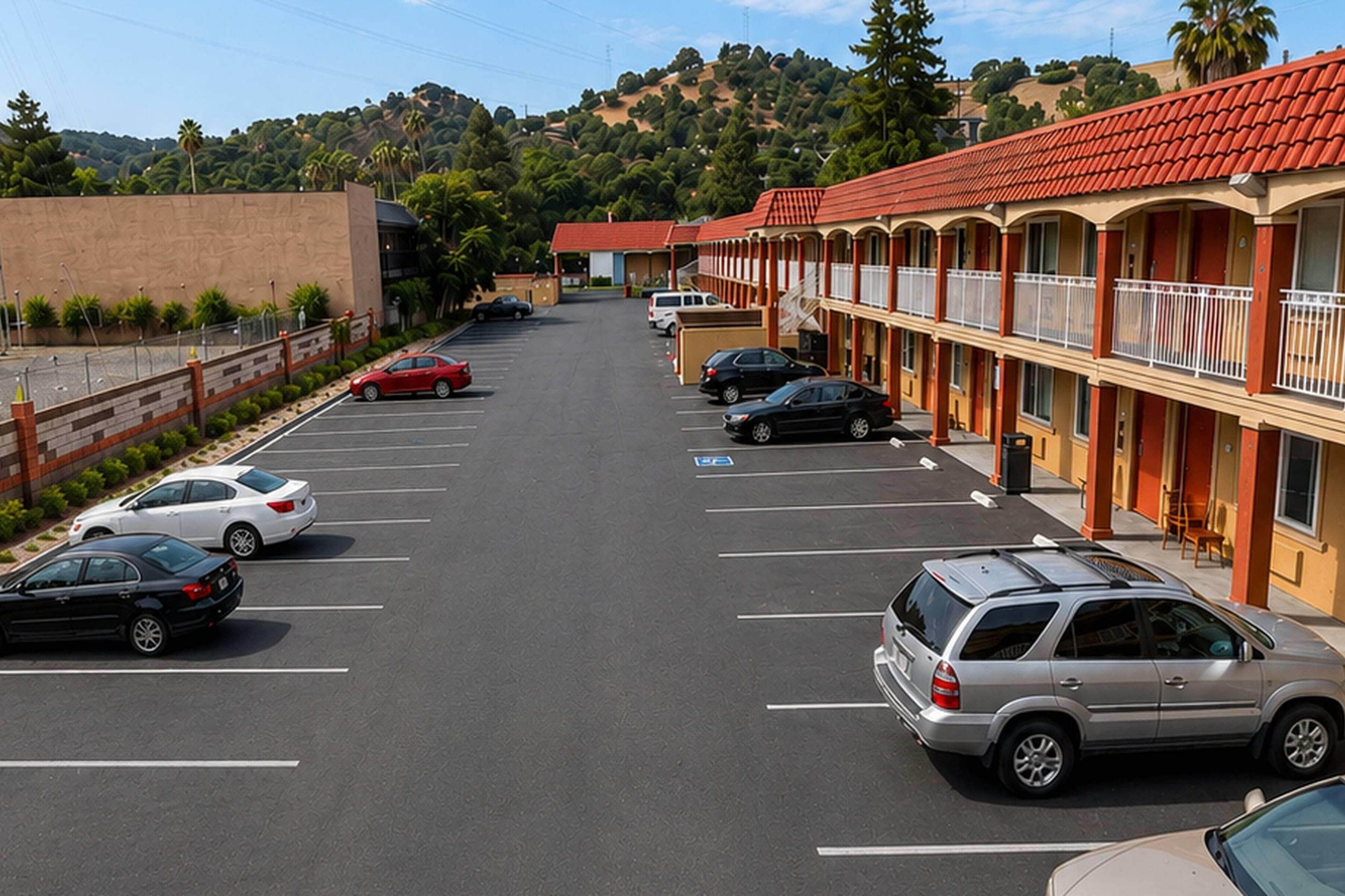 A parking lot with multiple cars, a building with a red roof, and a hilly landscape in the background.