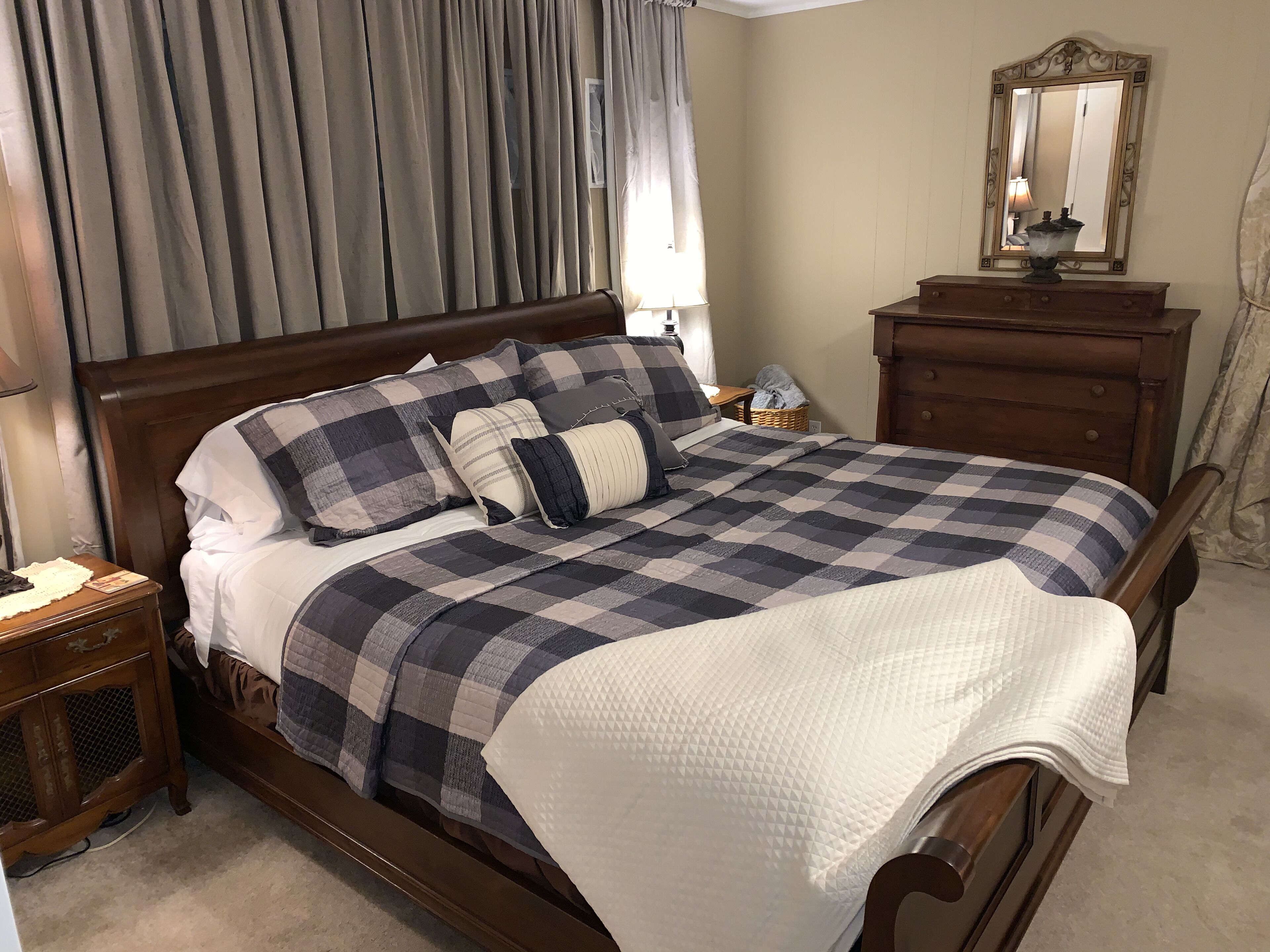 Una cama bien hecha con un edredón a cuadros, un cabecero de madera y una mesita de noche con una lámpara.