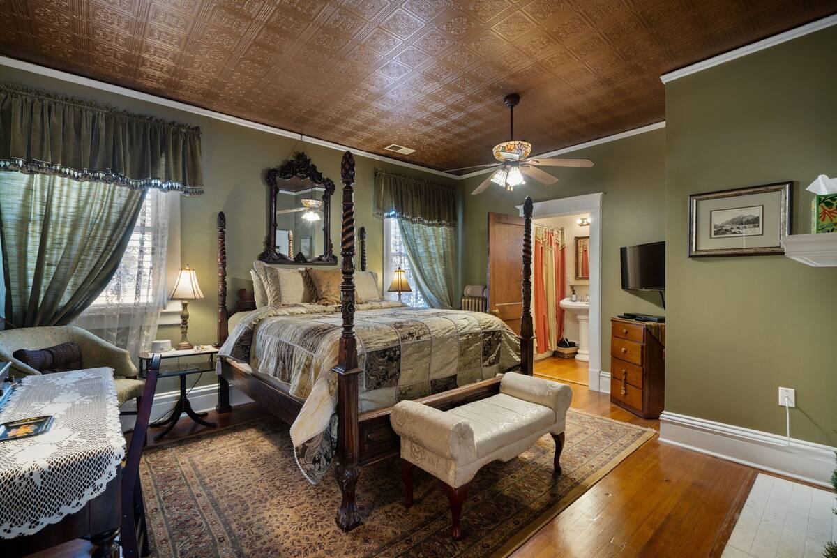 A traditional bedroom with a four-poster bed, a ceiling fan, and a wooden floor.