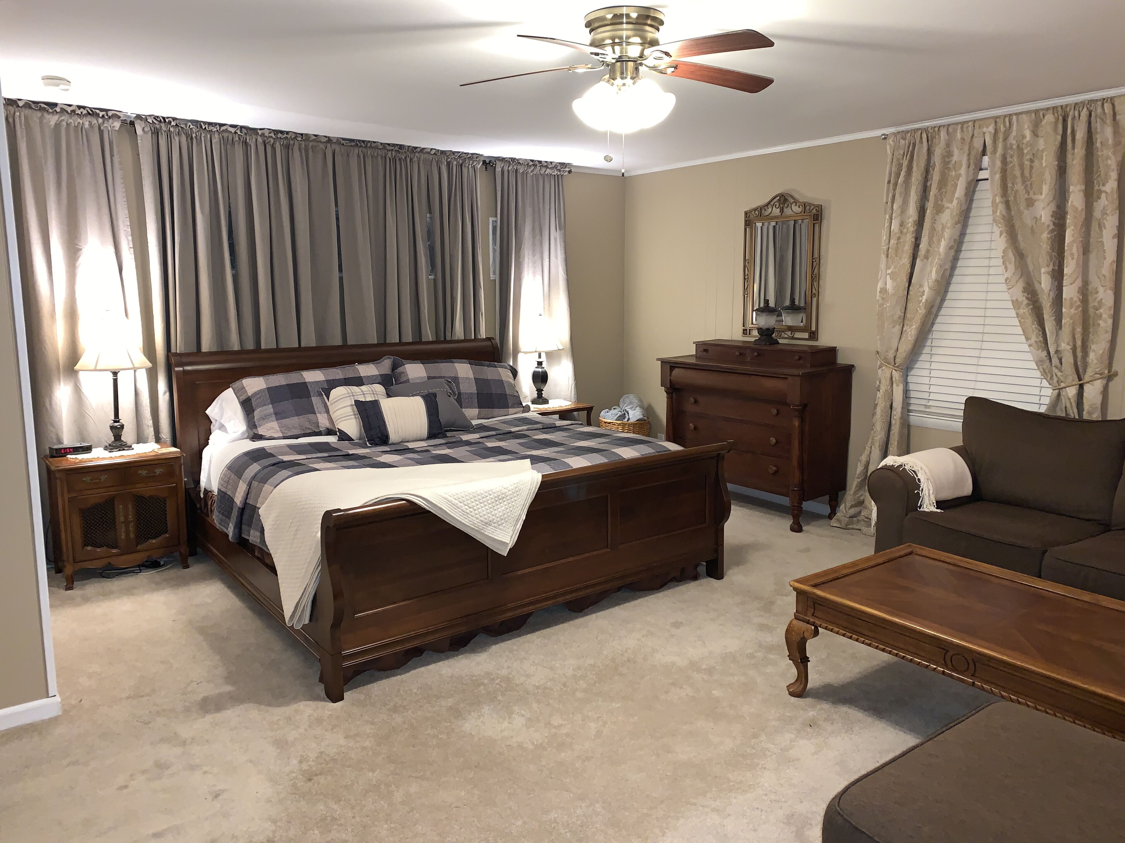 A bedroom with a large bed, a dresser, a nightstand, a ceiling fan, and a window with curtains.