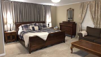 A bedroom with a large bed, a dresser, a nightstand, a ceiling fan, and a window with curtains.