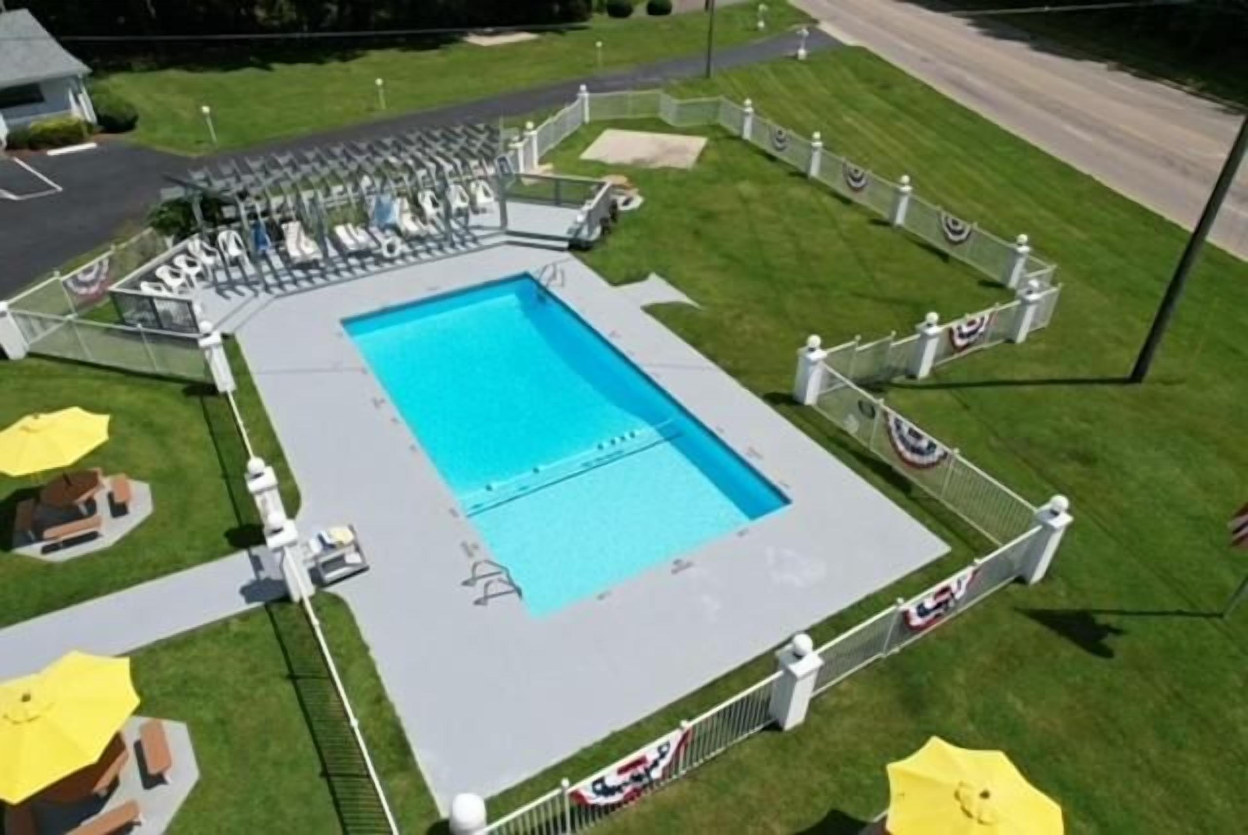 Una piscina rectangular envoltada per una tanca blanca, amb gandules i ombrelles al voltant.