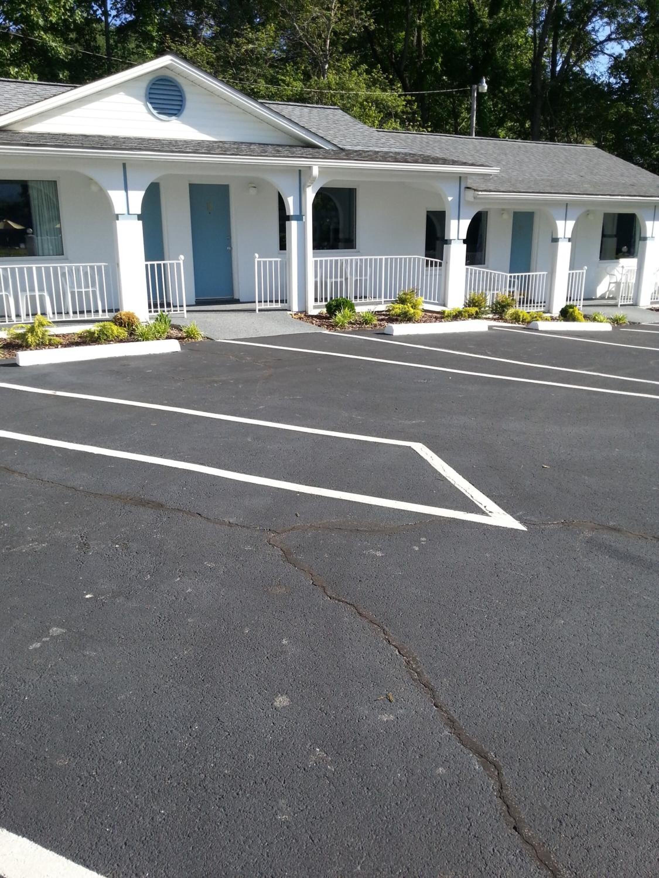 A motel with a central entrance, a covered parking area, and a row of rooms with a blue door.
