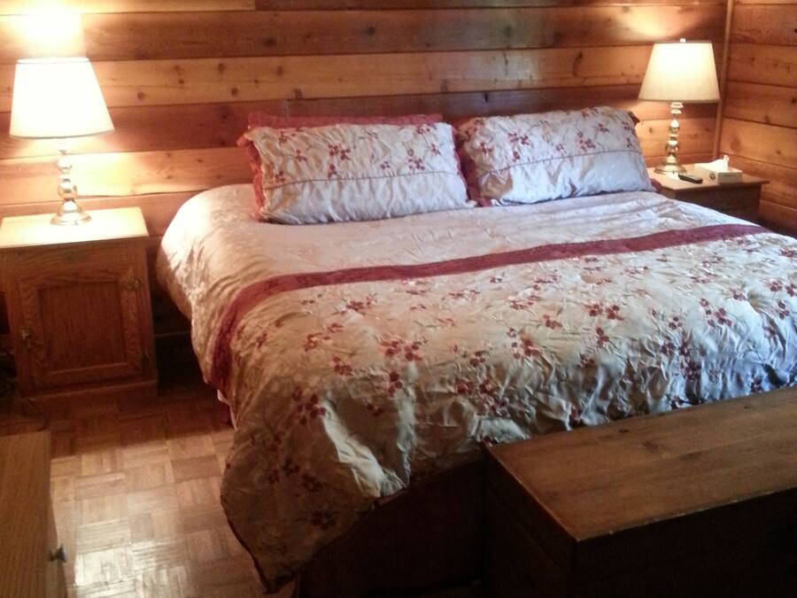A wooden-paneled room with a bed, two bedside tables, and a bench.