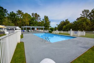 Una piscina con area relax coperta, circondata da un recinto bianco e alberi.
