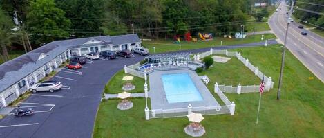 A motel with a swimming pool, parking lot, and a road in the background.