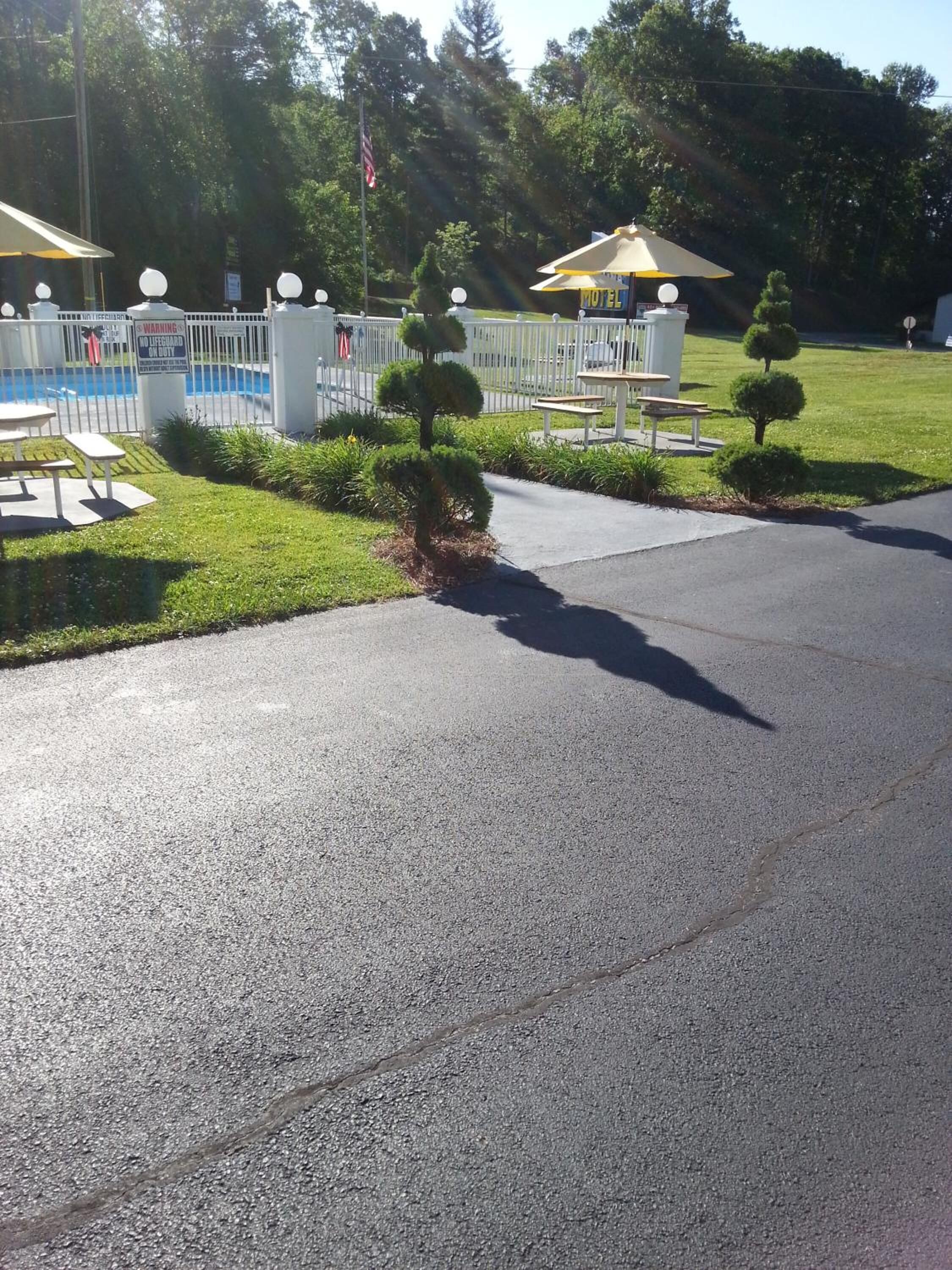 A motel with a fenced pool area, a small garden with trimmed bushes, and a picnic table.