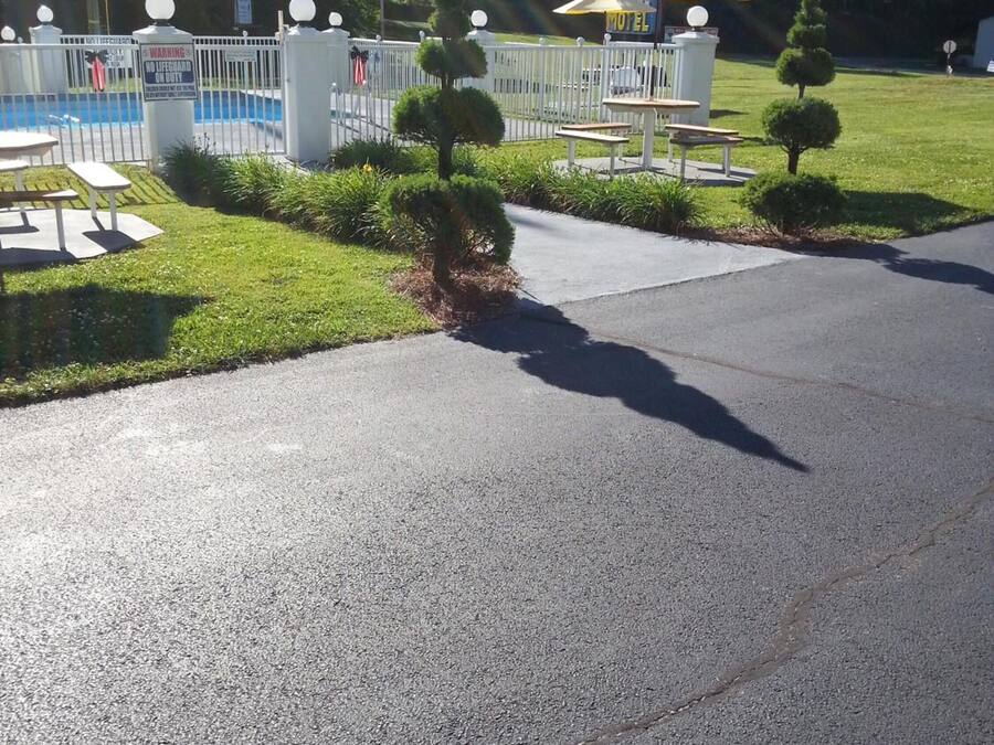 A motel with a fenced pool area, a small garden with trimmed bushes, and a picnic table.