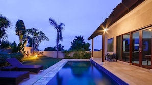 A swimming pool with lounge chairs and a patio area with a table and chairs.