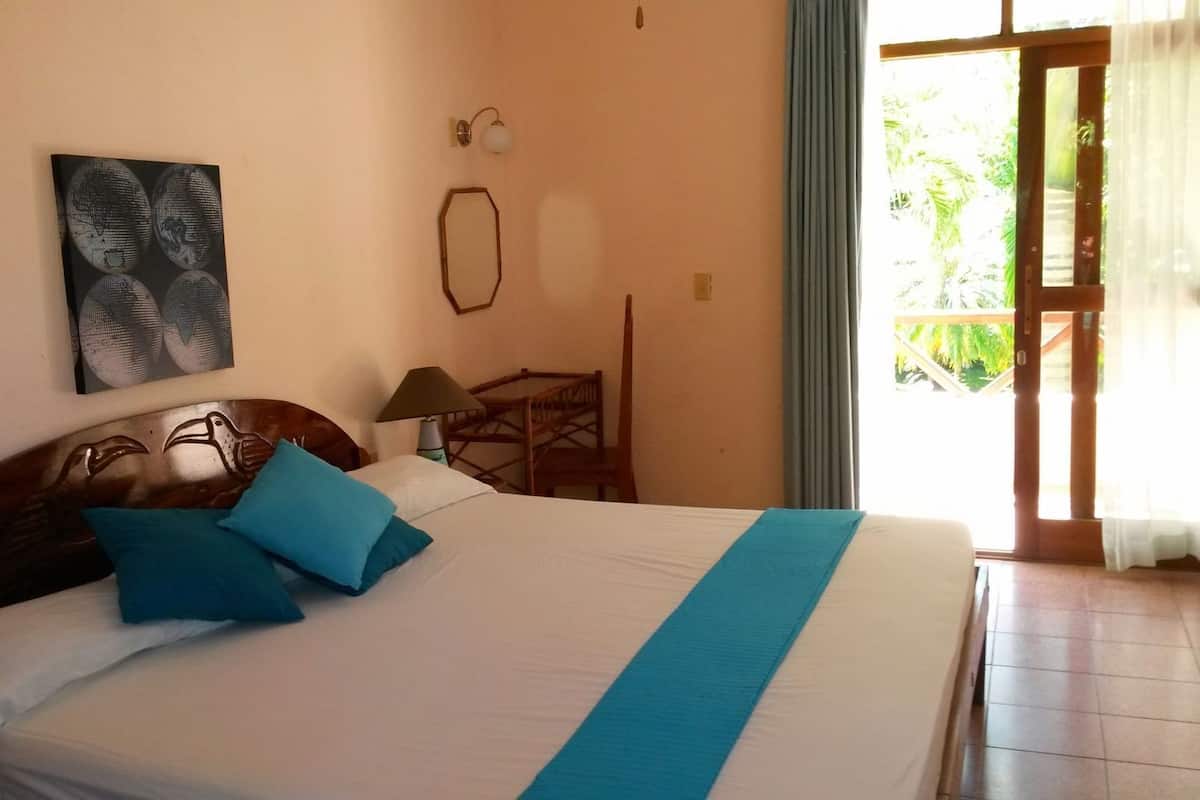 Een hotelkamer met een bed, een bureau, een stoel, een lamp en een raam met gordijnen.