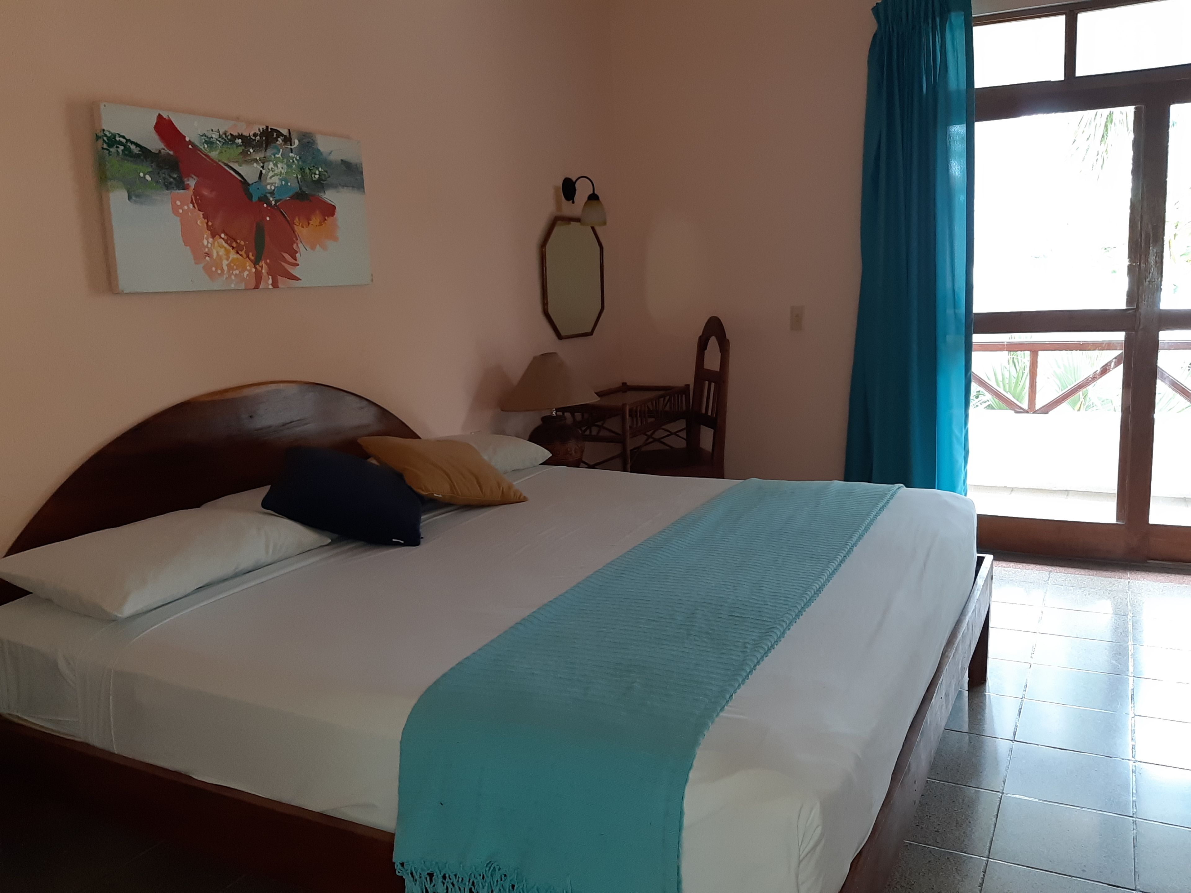 Une chambre à coucher avec un lit, des oreillers, un tableau, une lampe, une chaise et une fenêtre avec des rideaux.