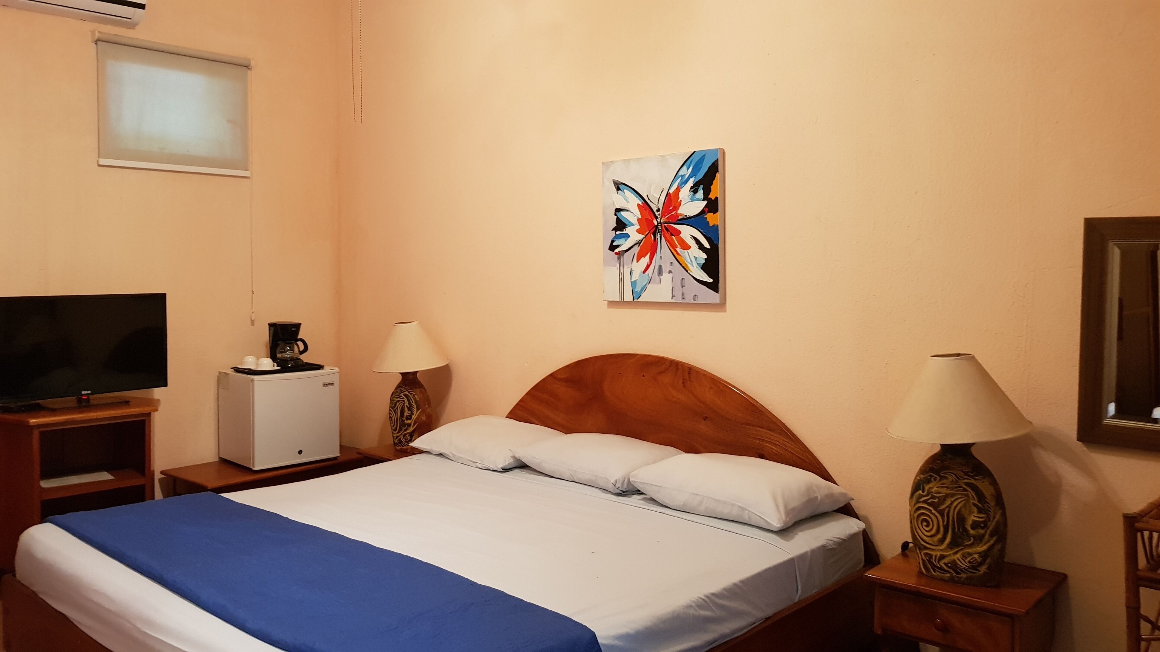 Ein Hotelzimmer mit einem Bett, zwei Nachttischlampen, einer Kaffeemaschine, einem Fernseher und einem Bild an der Wand.