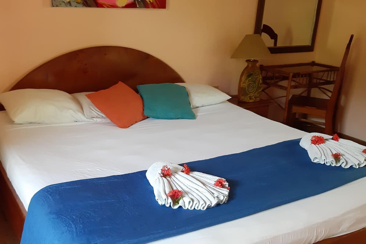 Een net opgemaakt bed met een blauwe sprei, witte lakens, twee decoratieve kussens en een blauw hoofdbord.