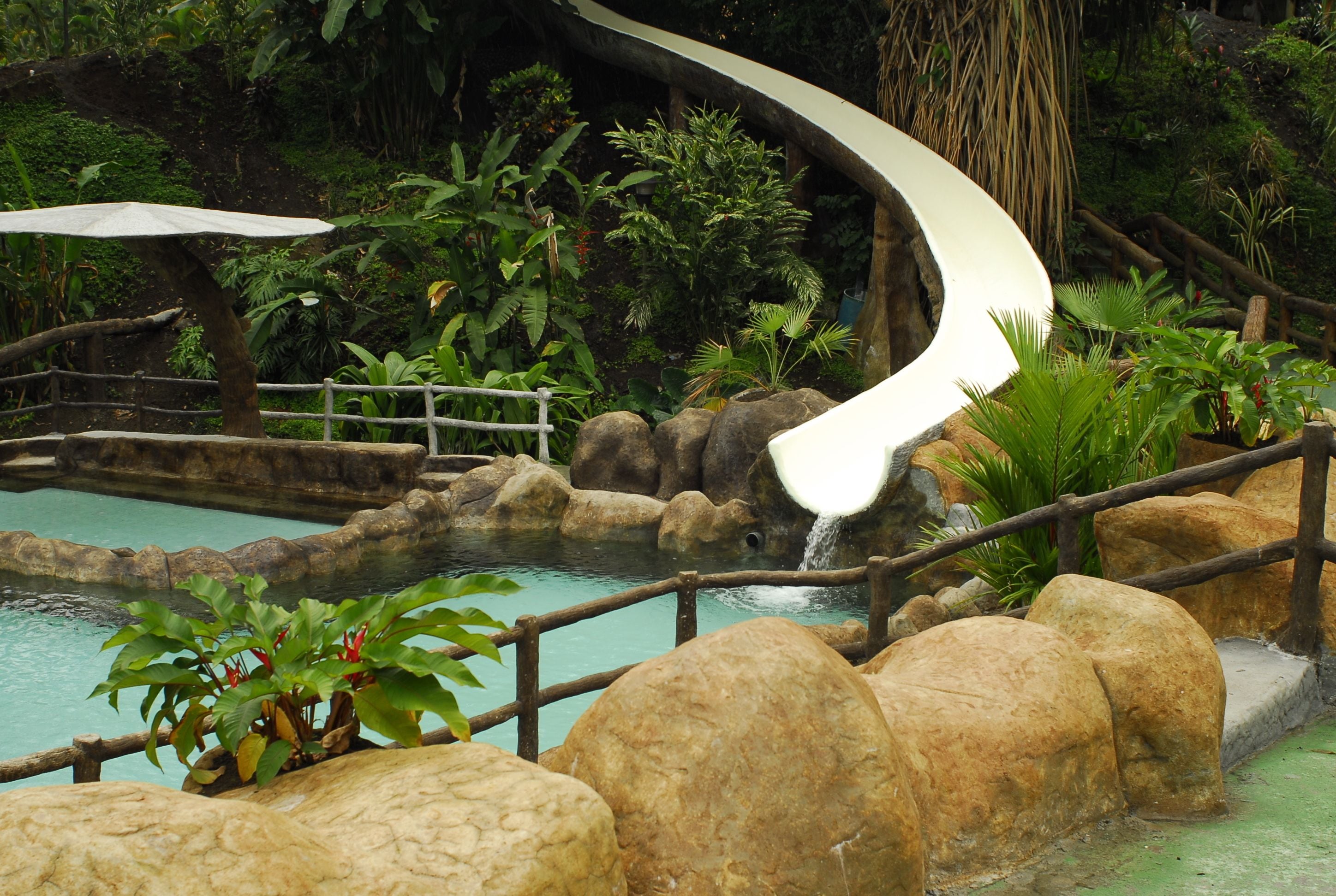 Tobogán de agua en un entorno tropical con piscina, rocas y exuberante vegetación.