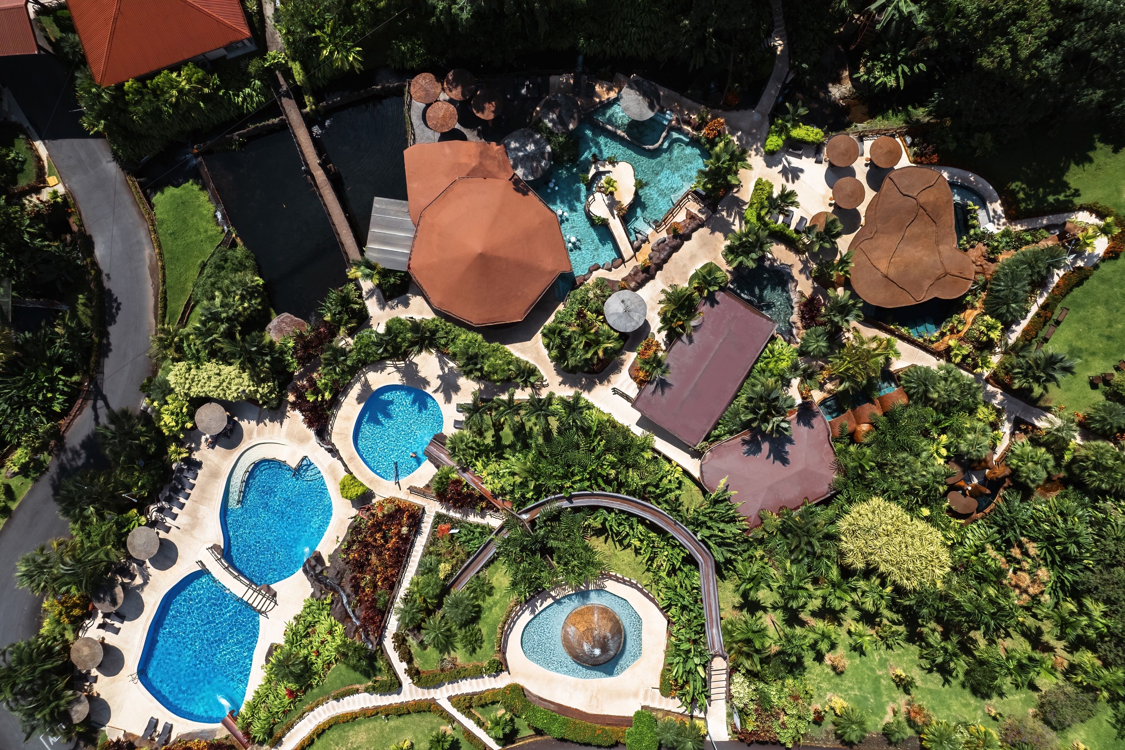 An aerial view of a resort with multiple swimming pools, a central fountain, and lush landscaping.