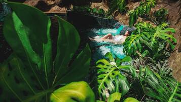 Une personne se détend dans une petite piscine naturelle, entourée de plantes tropicales.