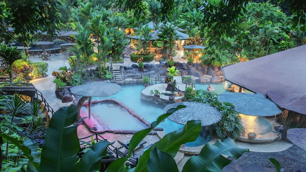 A lush, tropical garden with a hot spring area, stone seating, and a variety of plants. - Hotel Los Lagos Spa & Resort (La Fortuna)