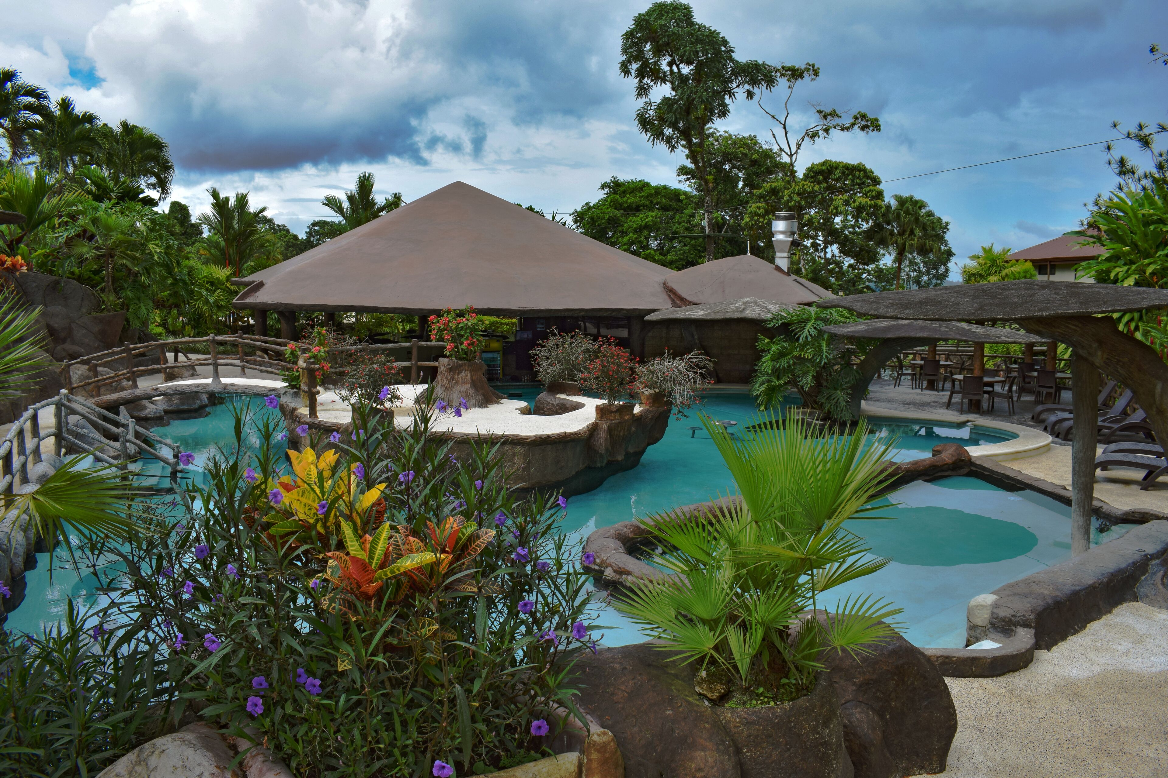 Un resort con varias piscinas, rodeado de exuberante vegetación tropical y zonas de estar cubiertas.