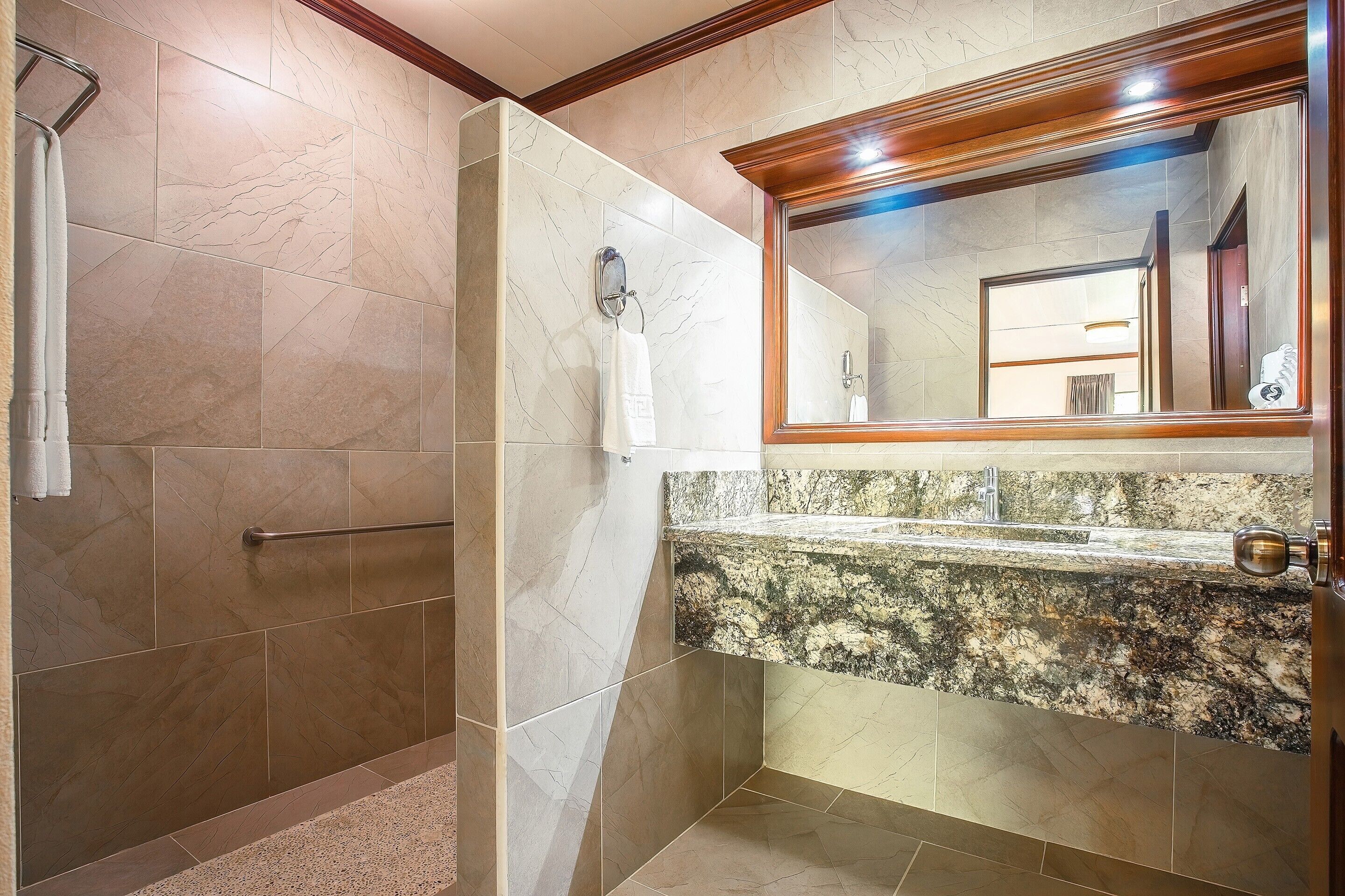 A bathroom with a shower, a towel rack, a mirror, and a granite countertop.