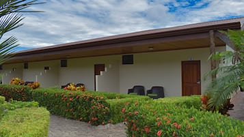 Un hotel con zona de estar exterior cubierta, un camino pavimentado y jardines bien cuidados.