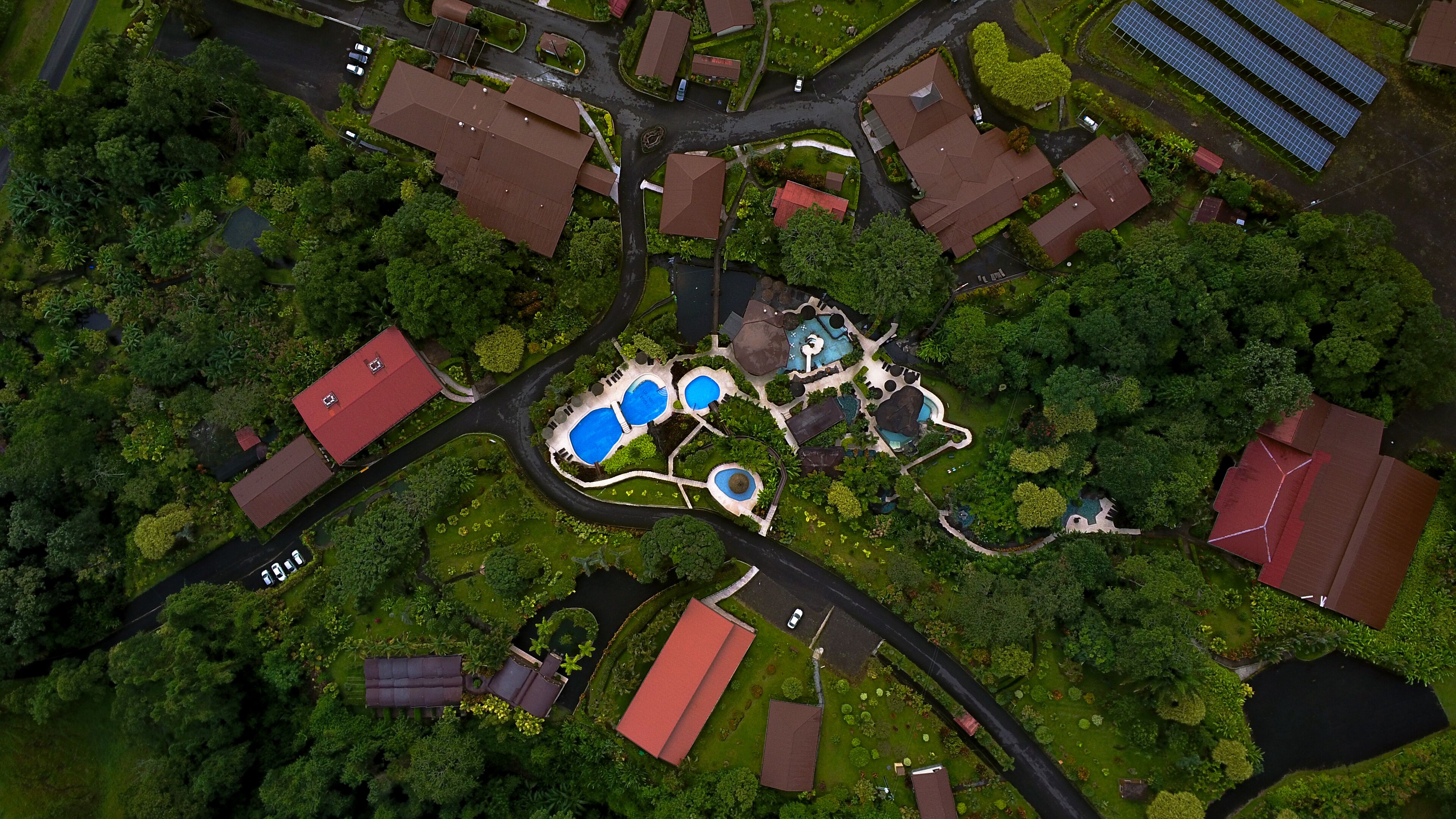 Vista aérea de una zona residencial con varias casas, un complejo de piscinas e instalaciones solares.