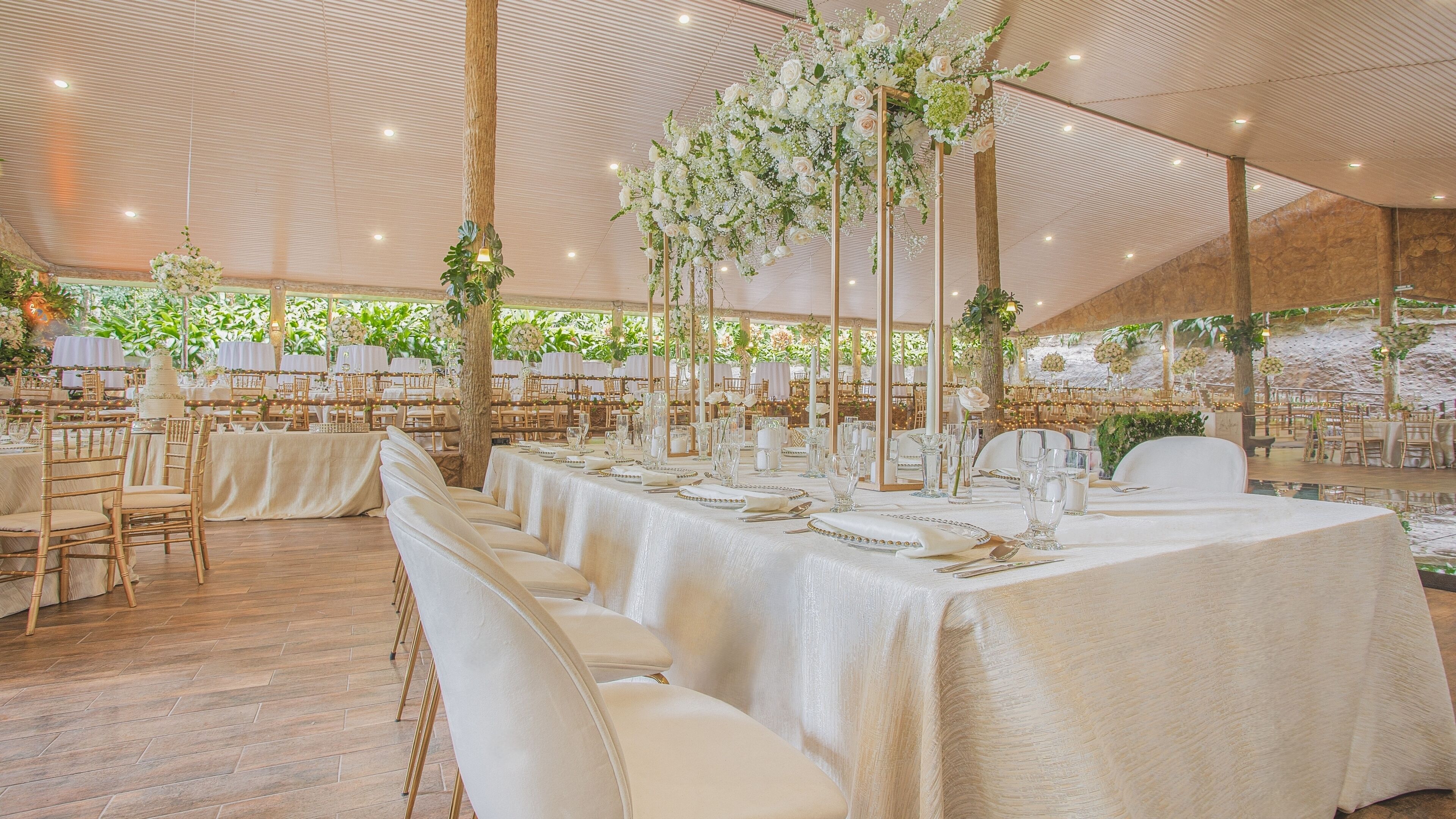 Un espace événementiel aménagé sous une tente, avec des tables dressées pour un événement formel, comprenant des nappes blanches et des centres de table floraux.