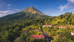 A mountain with a red-roofed building complex at its base, surrounded by lush greenery. - Hotel Los Lagos Spa & Resort (La Fortuna)