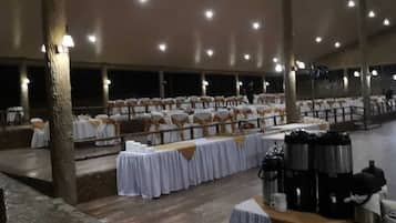A banquet hall with rows of tables covered in white tablecloths, chairs with white and gold sashes, and a coffee station.