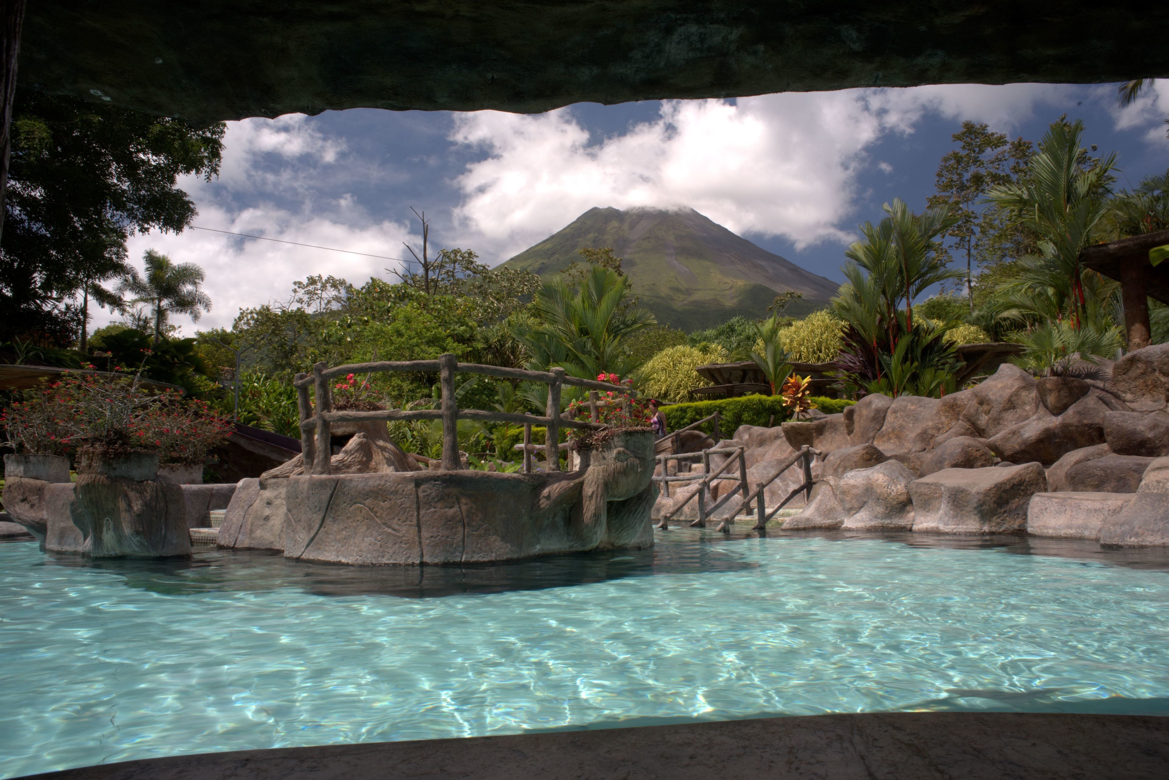 A pool with clear water, surrounded by rocks and plants, with a view of a mountain in the background.