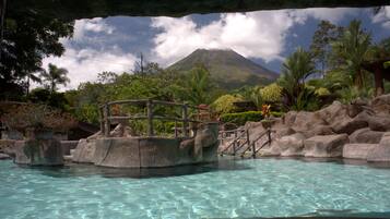 A pool with clear water, surrounded by rocks and plants, with a view of a mountain in the background.