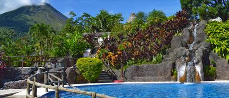 A pool area with a wooden bridge, a waterfall, and a mountain in the background.