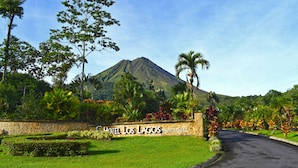 A landscaped entrance with a sign for Hotel Los Lagos Spa & Resort, surrounded by tropical vegetation and a mountain in the background. - Hotel Los Lagos Spa & Resort (La Fortuna)